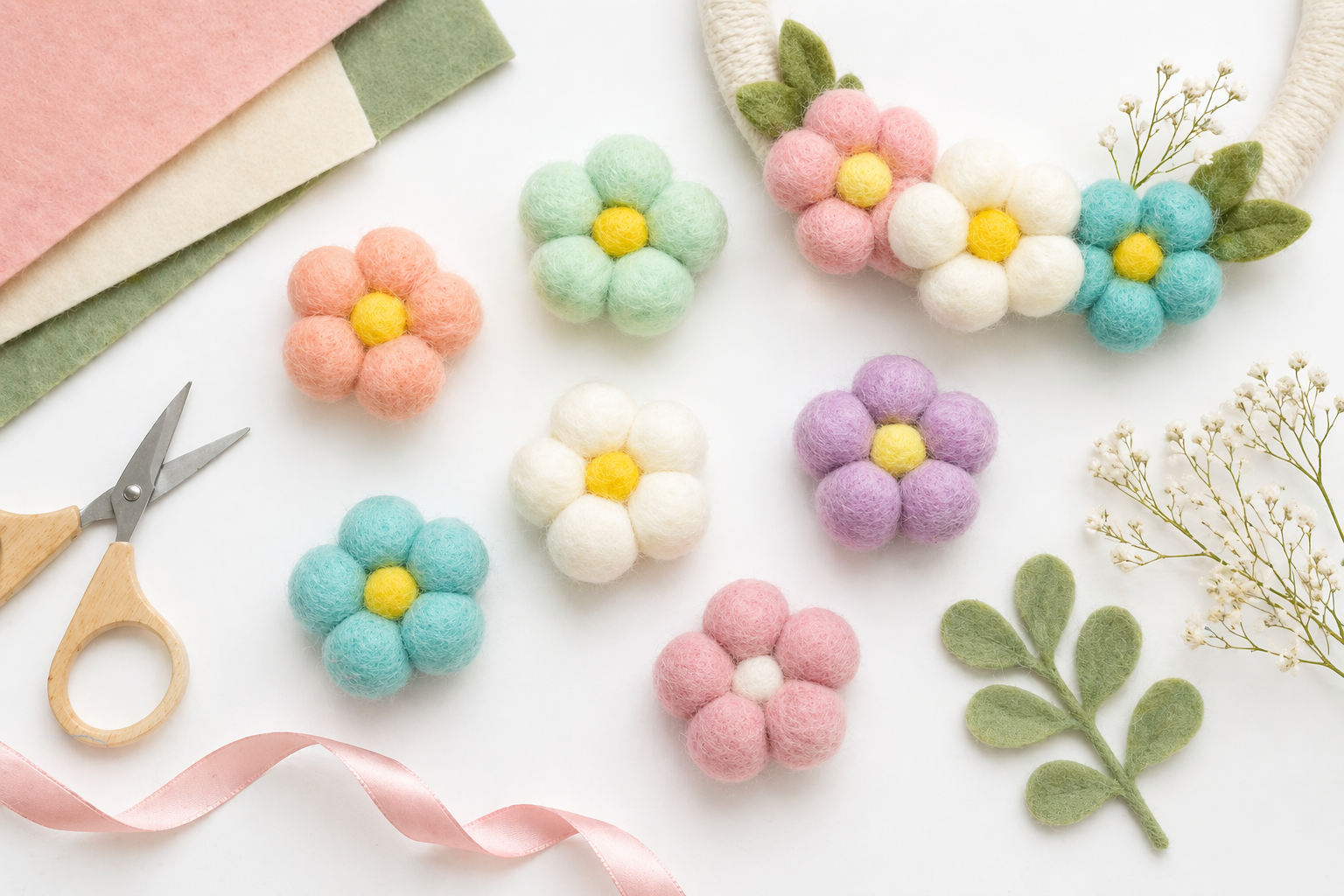 Flat lay of pastel wool felt flowers, scissors, felt sheets, and a half-finished wreath on a bright table